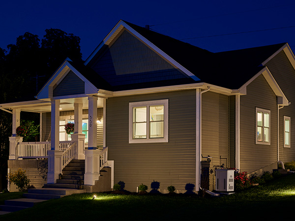 A standby generator next to a home with all its lights on at night