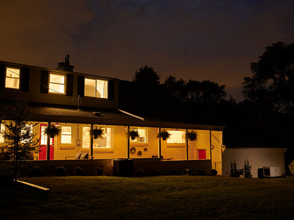 Standby generator in front of lit house at night.