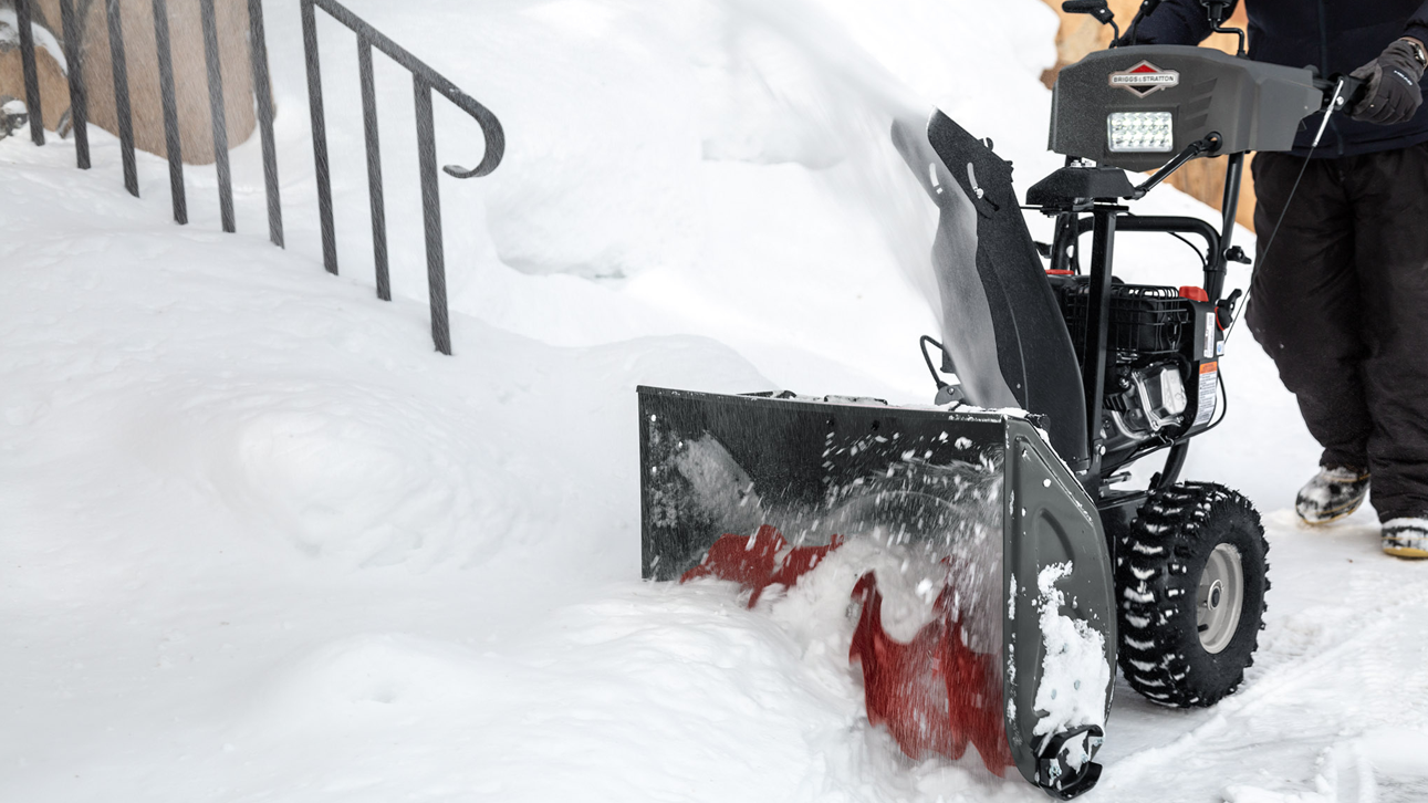 Person pushing a snow blower powered by a Briggs &amp; Stratton Snow Series Single-Cylinder Horizontal Shaft engine